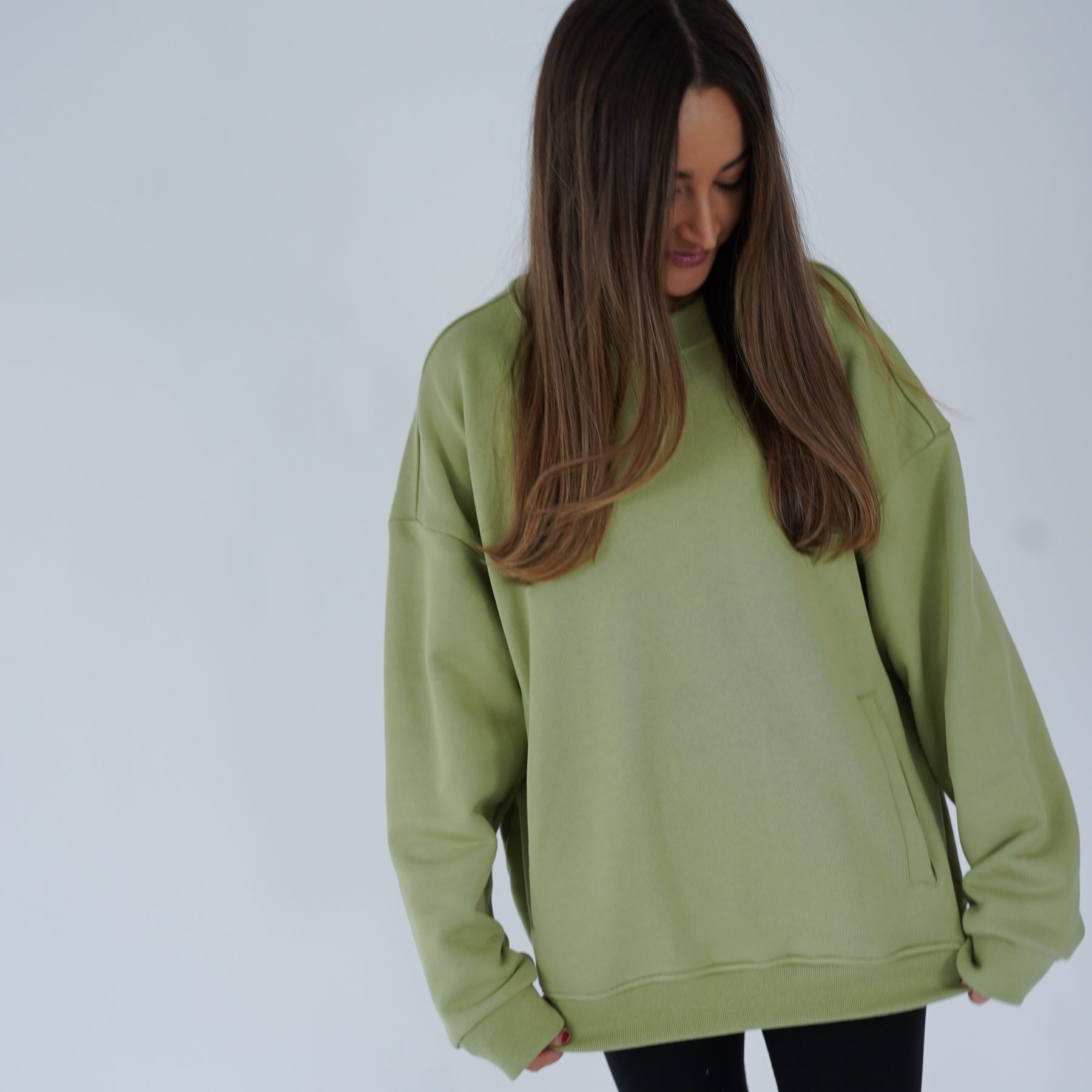 Woman wearing a green crewneck with pocket, looking down